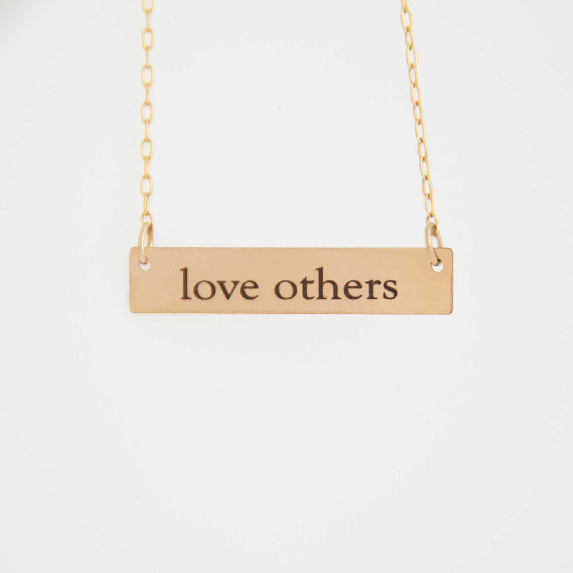 The 1.25 inch rectangle bar necklace is hung from above with love others engraved in the ol' serif font.