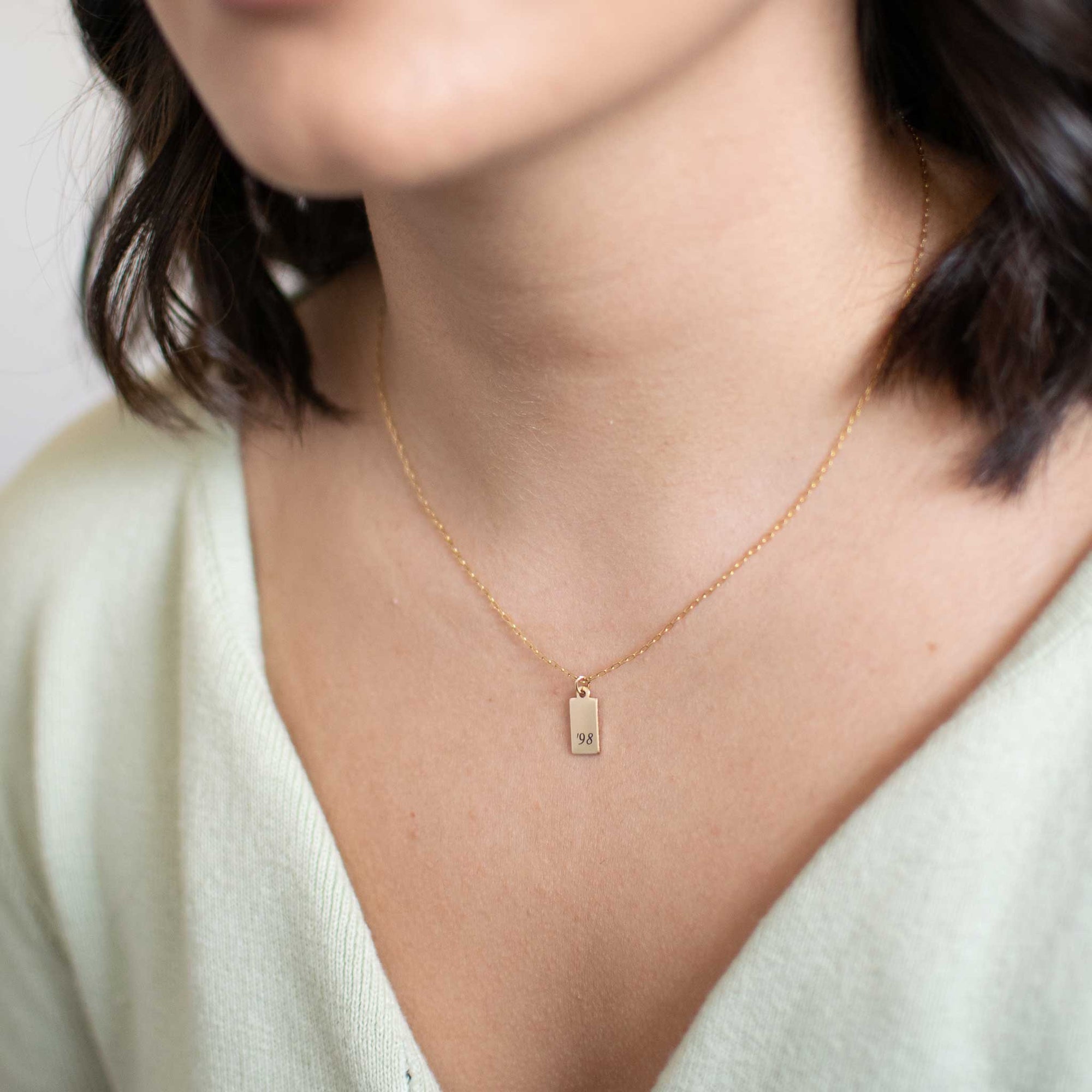A close up of the tag necklace with '98 engraved horizontally.