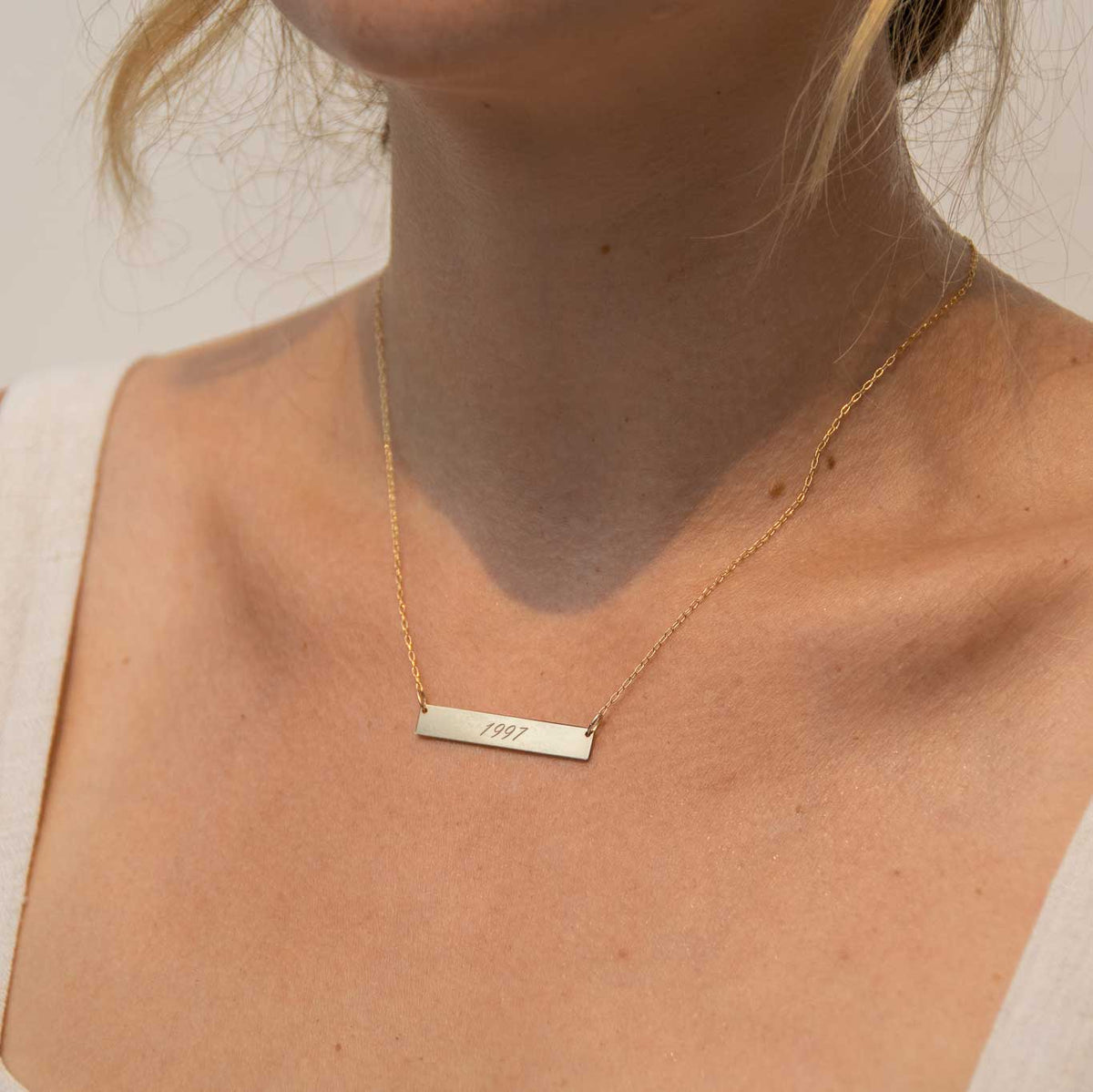 Rectangle bar necklace worn by a woman. The rectangle has 1997 engraved with the script font