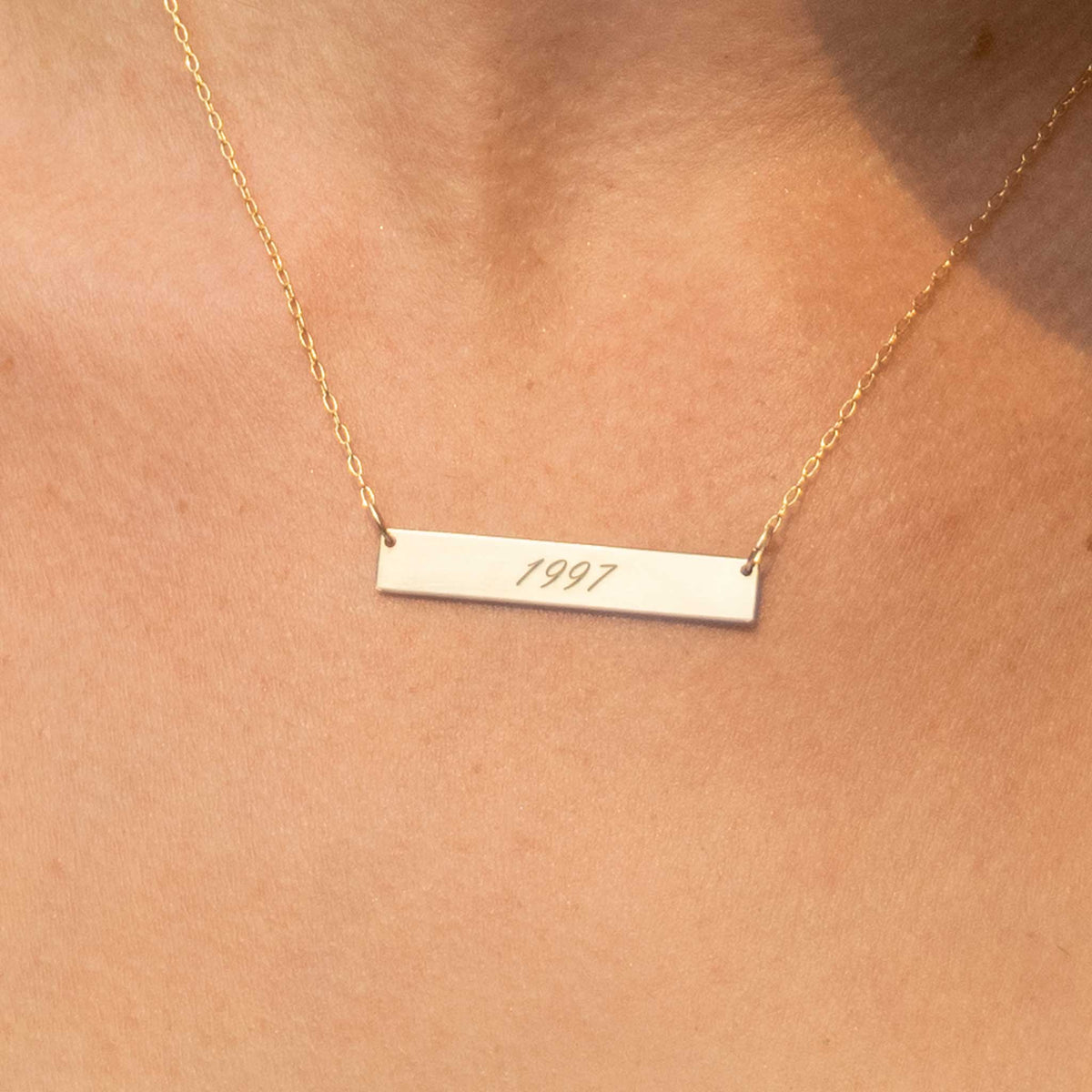 A close up of the rectangle necklace being worn. The neckace has 1997 engraved in a script font. 