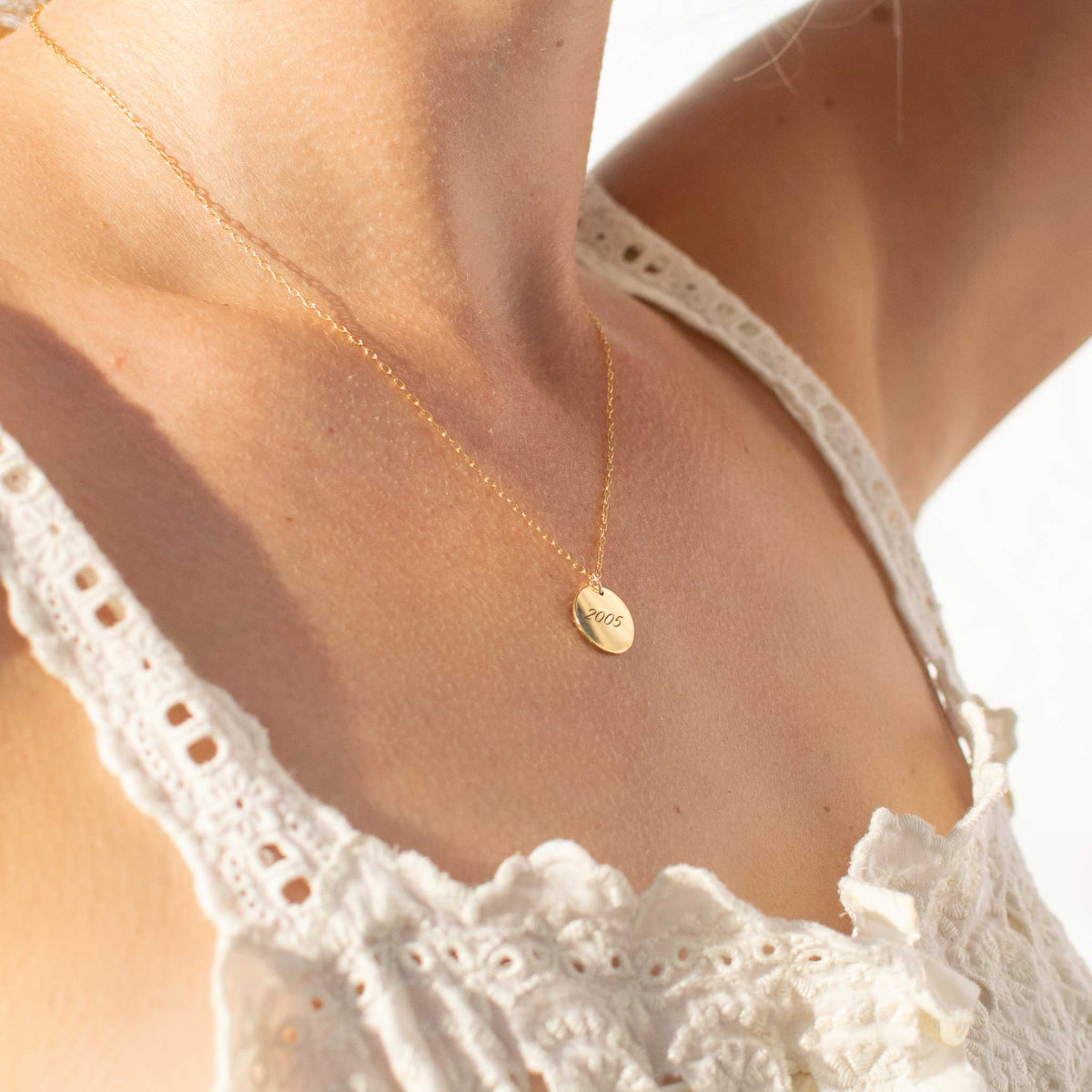 A view of a woman wearing a 13mm disk pendant from a right angle viewpoint. The necklace has 2005 engraved with the script font. 