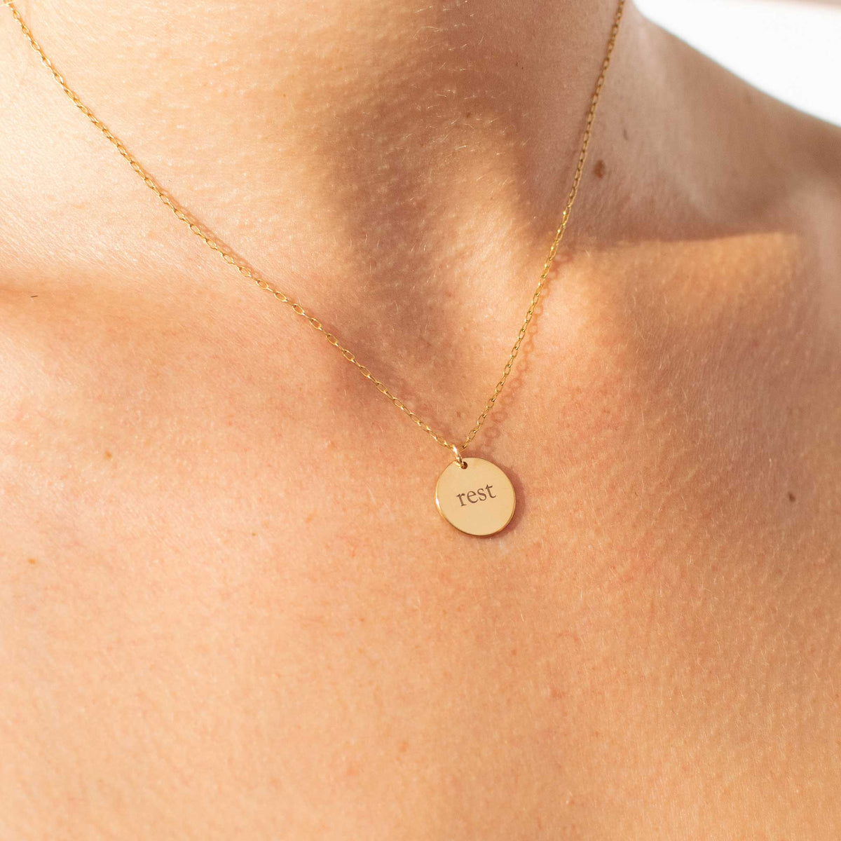a very close up of the gold 13mm circle pendant with rest engraved using the ol&#39; serif font. Image is focused on just necklace with only a small part of neck and chest showing.