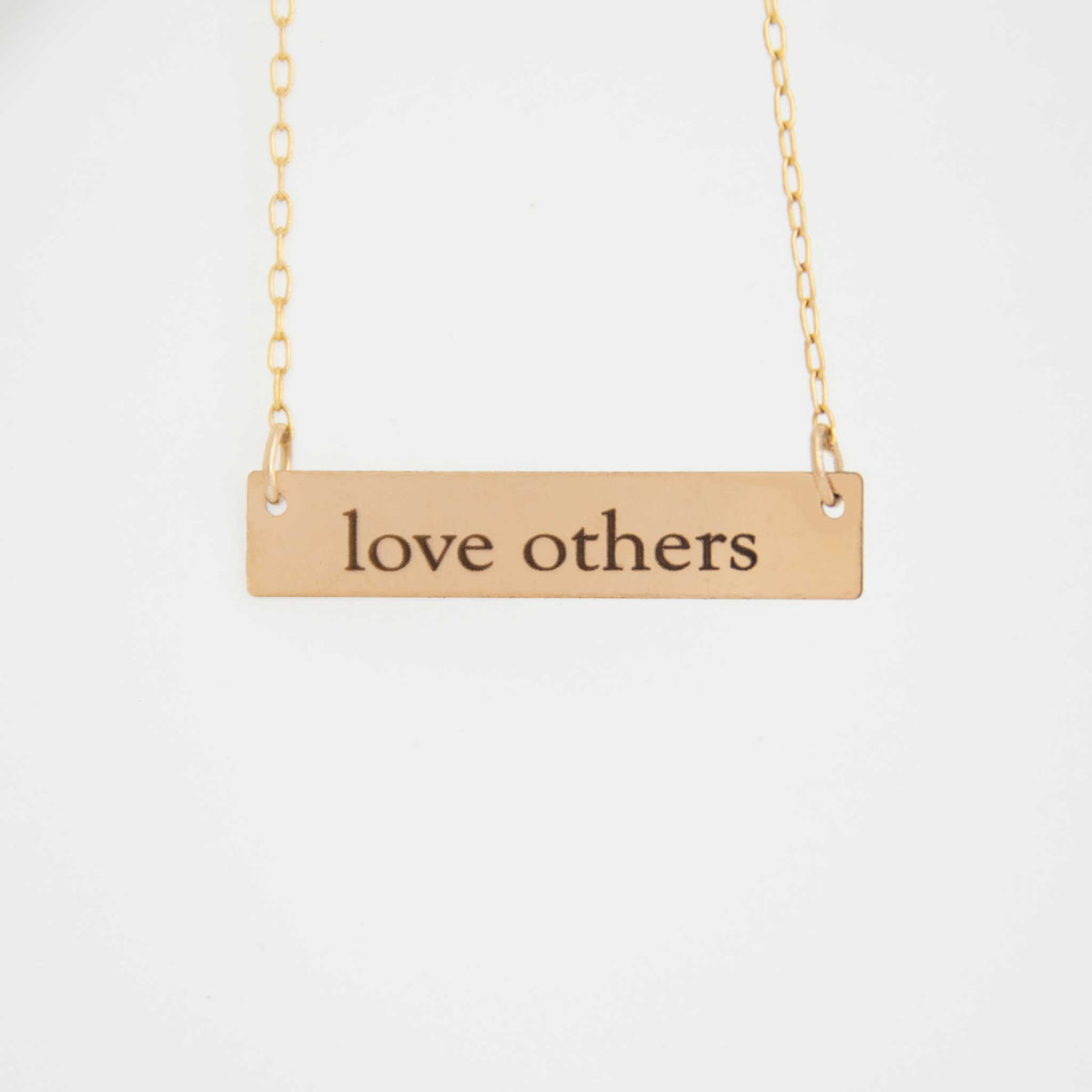 The 1.25 inch rectangle bar necklace is hung from above with love others engraved in the ol&#39; serif font.