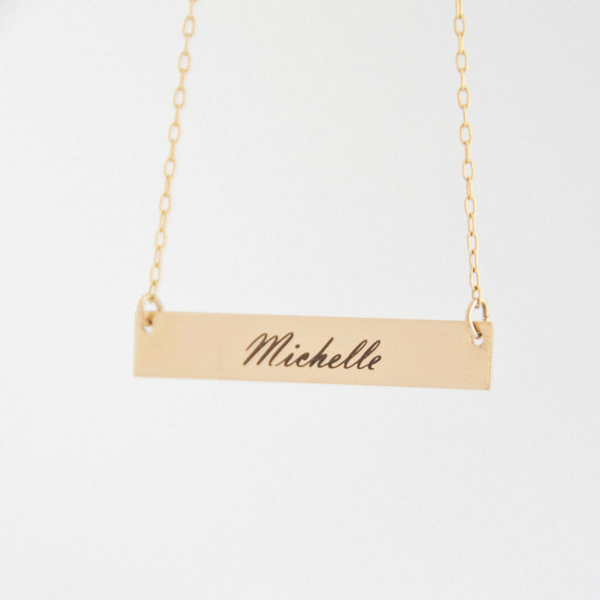 The rectangle bar necklace with Michelle engraved with script font in front of a white background. 