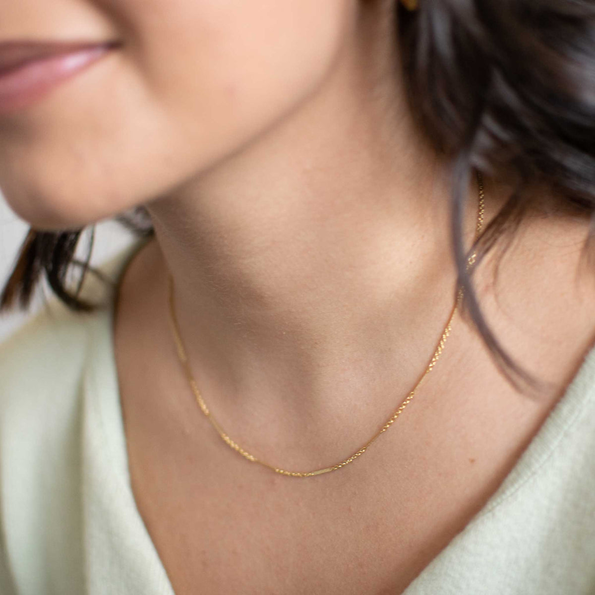 The gold necklace worn by a woman from a slight right angle.