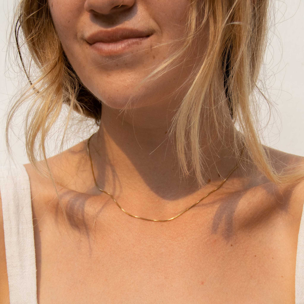 A woman with messy hair wearing just the gold box chain. Only from the nose down is shown.