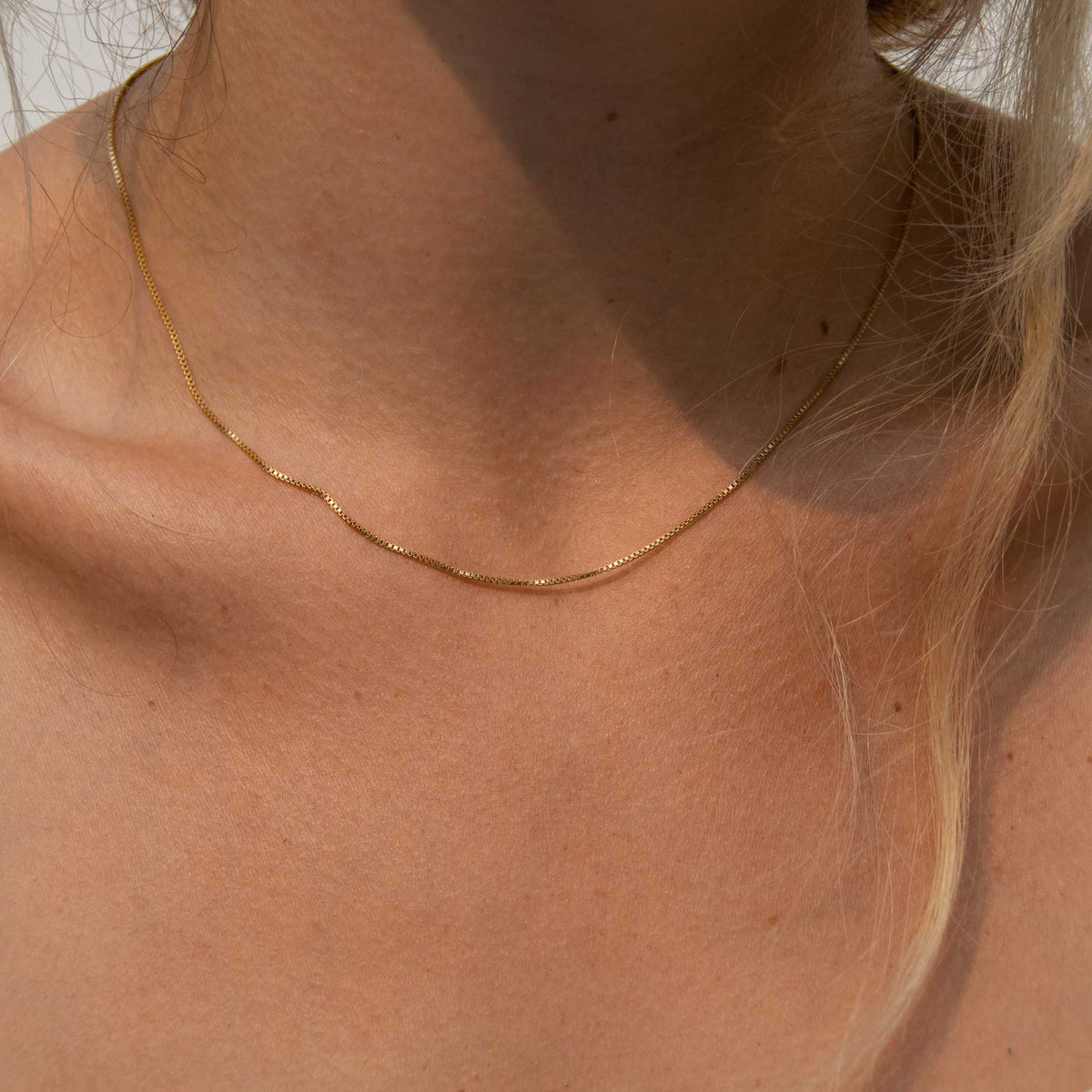 Close up of the necklace with piece of hair hanging down and a shadow from face on the right side of the image.