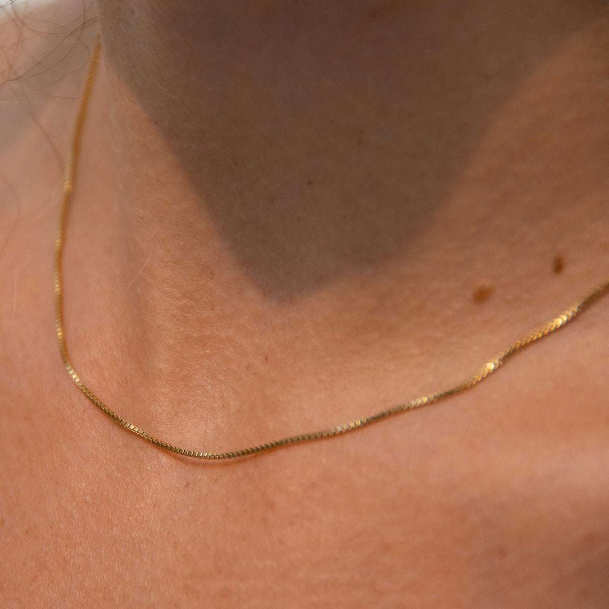 A very up close shot of the box chain necklace with only part of the necklace in focus to highlight the small details.