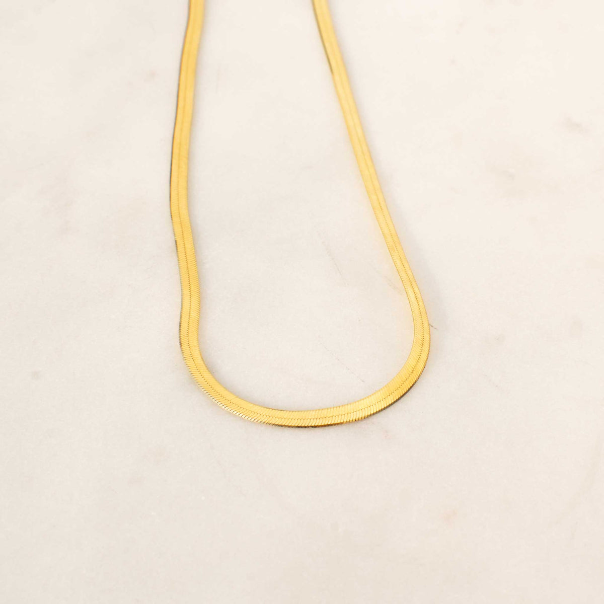 Half of the herringbone necklace laid on a white background forming a U shape. 