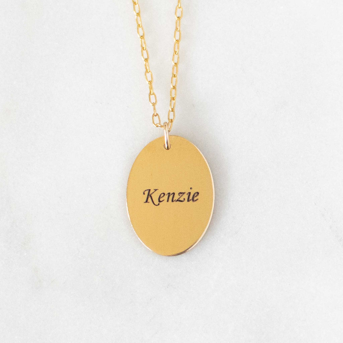 Gold Oval pendant with Kenzie engraved on a solid white background.