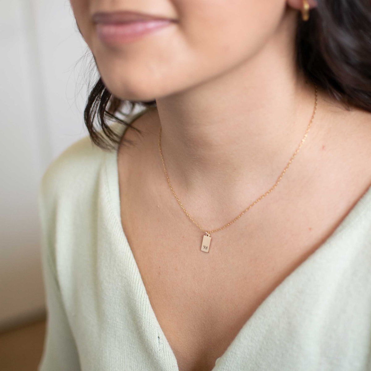 A woman wearing the gold tag necklace with&#39;98 engraved in the ol&#39; serif font.