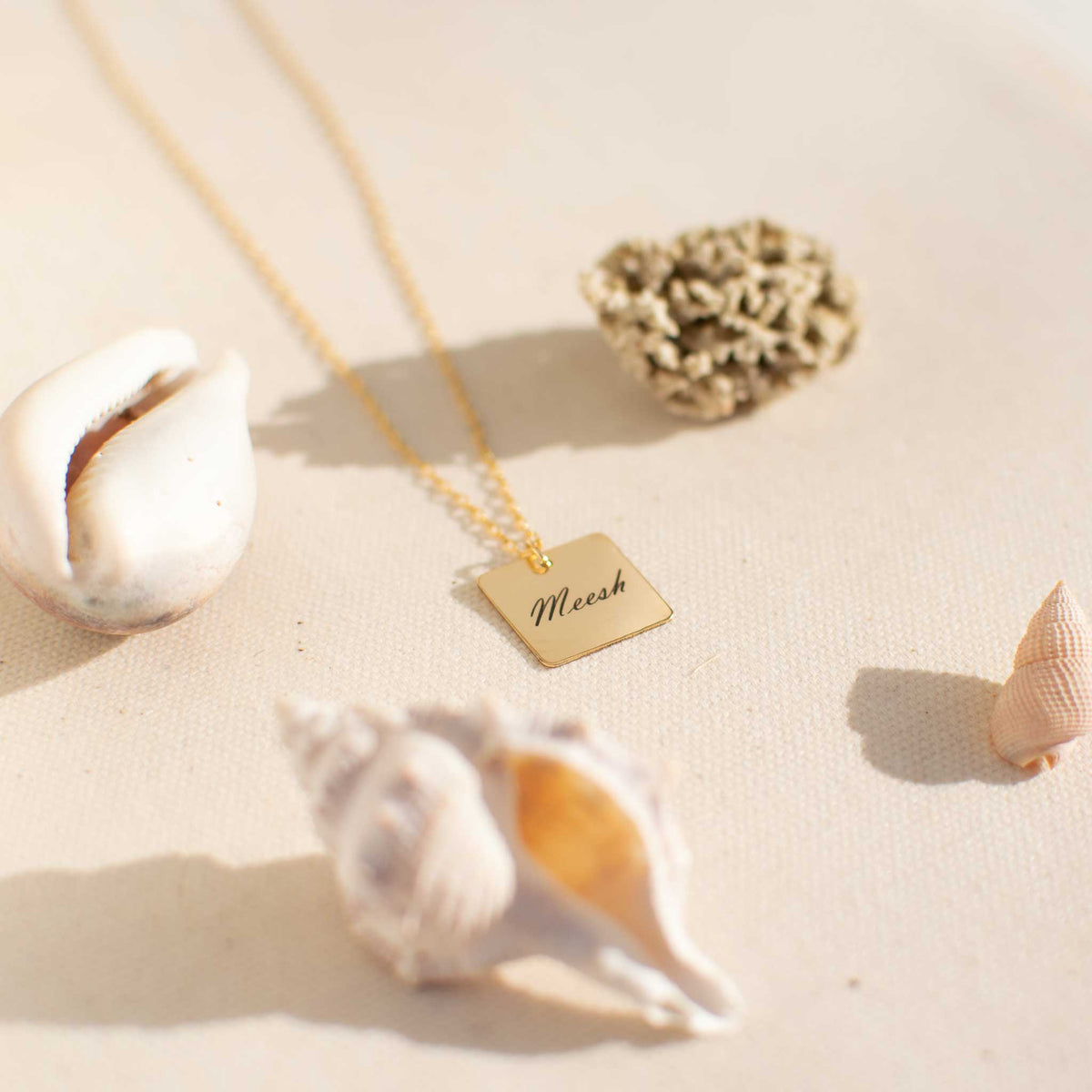 A square necklace laying on a white textured board with four seashells located on each corner of the screen. 