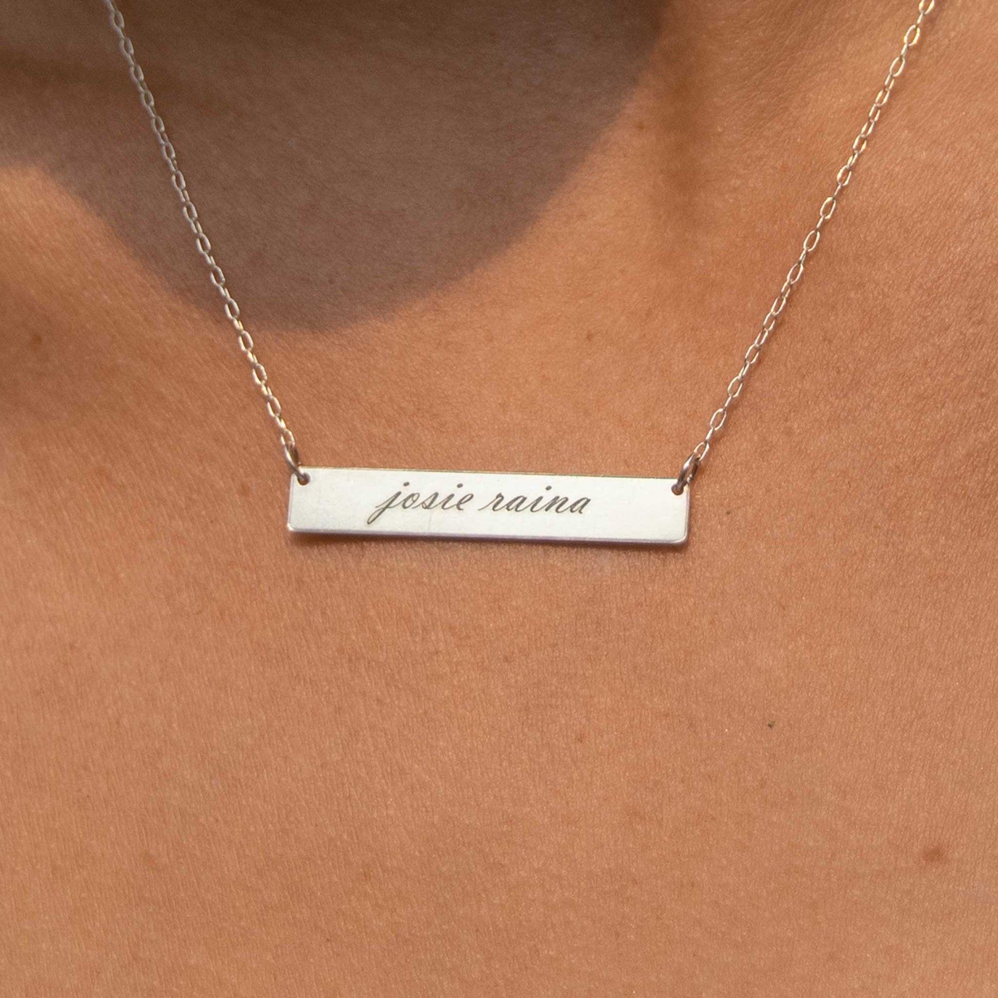 Close up of the 1.5" silver rectangle necklace with Josie Raina engraved in the script font. 