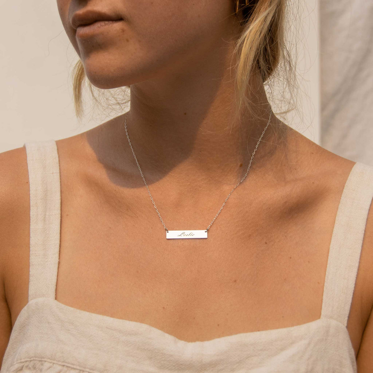 Woman wearing the silver rectangle bar necklace with Leslie engraved. 