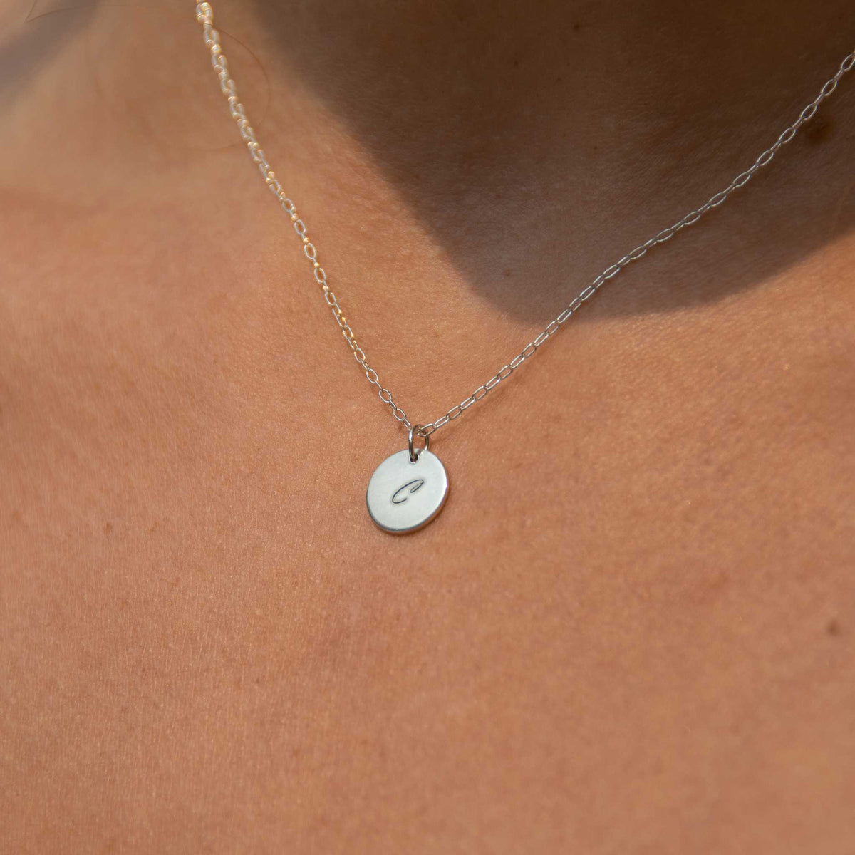 Up close of the silver disk necklace engraved with the script font. 