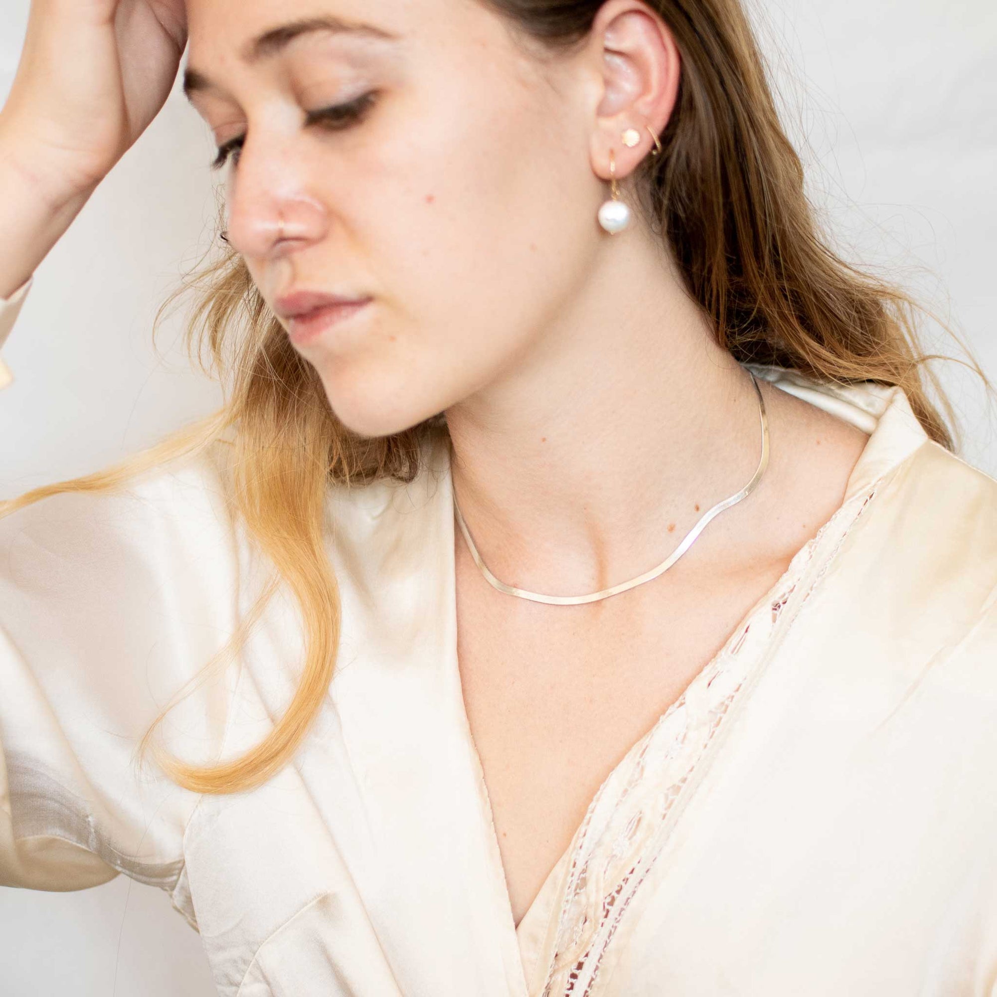 Woman wearing a thick silver herringbone chain. Model is looking down wearing a v neck silk blouse. 