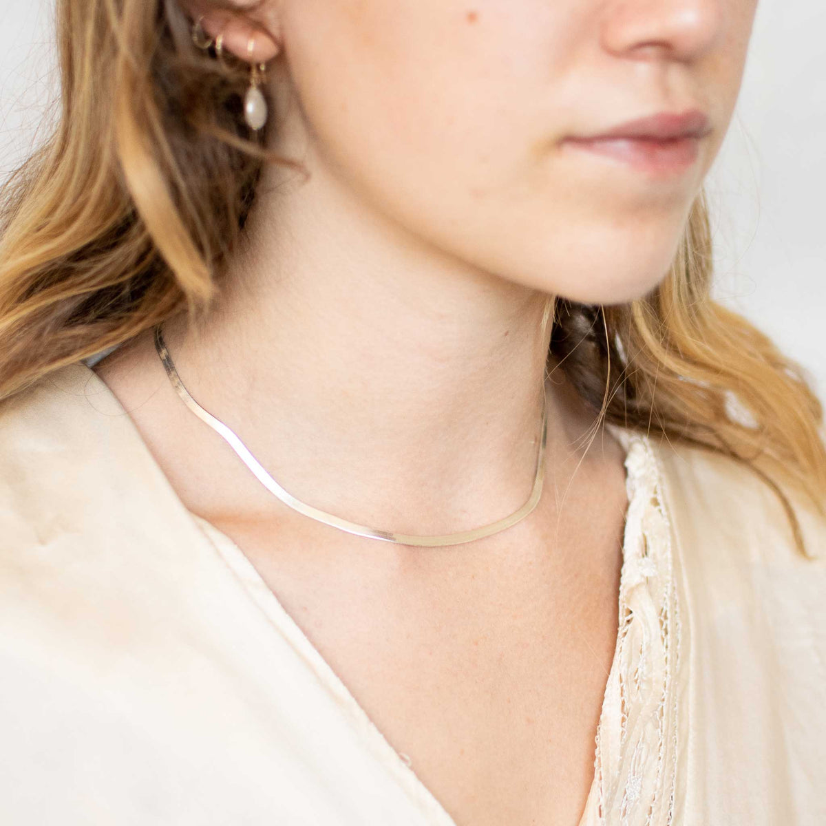 model wearing silver herringbone necklace in a close up shot. 