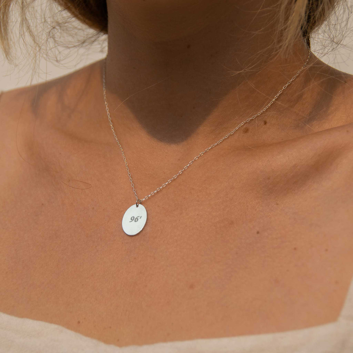 up close of model wearing a silver oval necklace with 96&#39; engraved.
