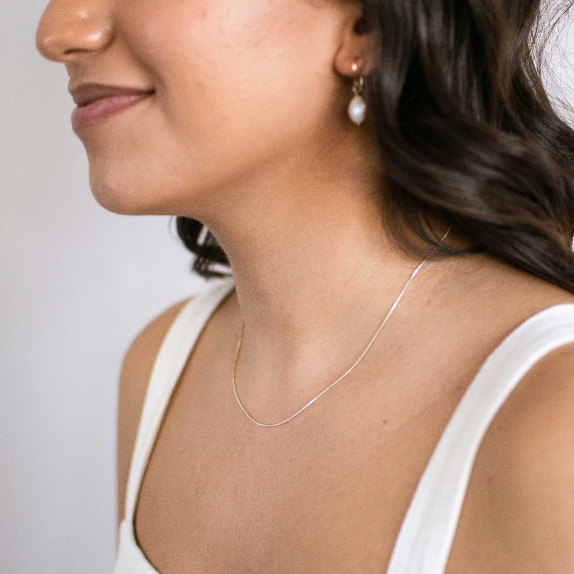 woman wearing a thin, silver box chain necklace from the left view.