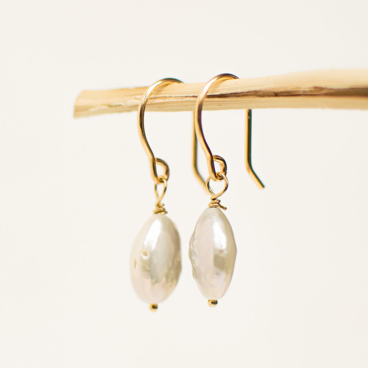 Two gold filled pearl drops hanging from a wooden stick.
