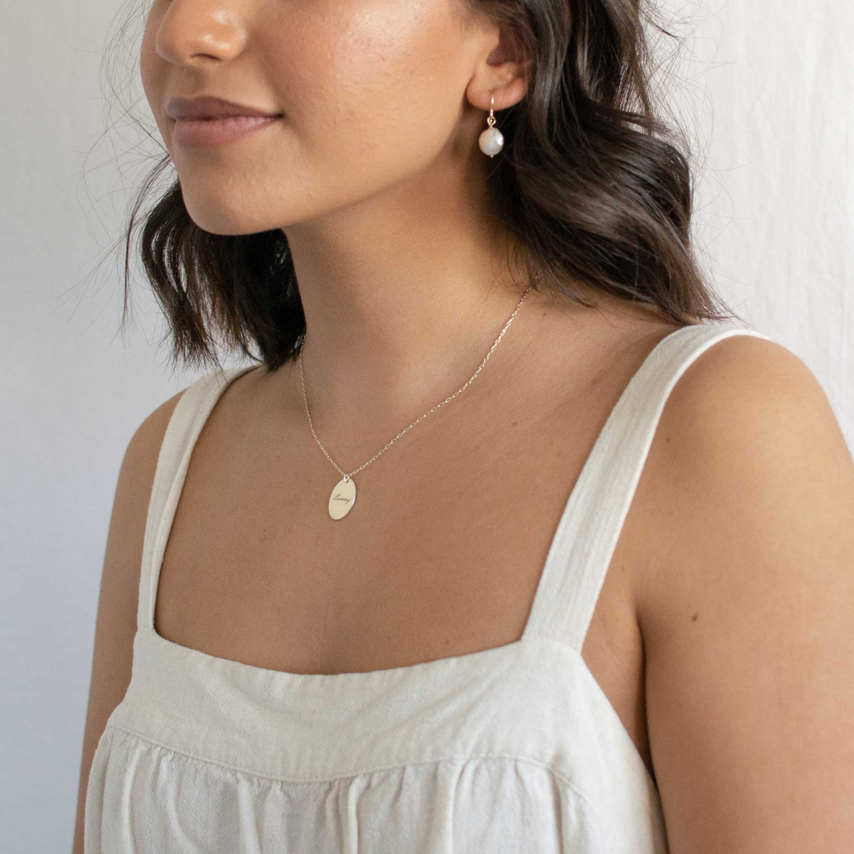 Model wearing a silver oval pendant necklace with a white tank top. 