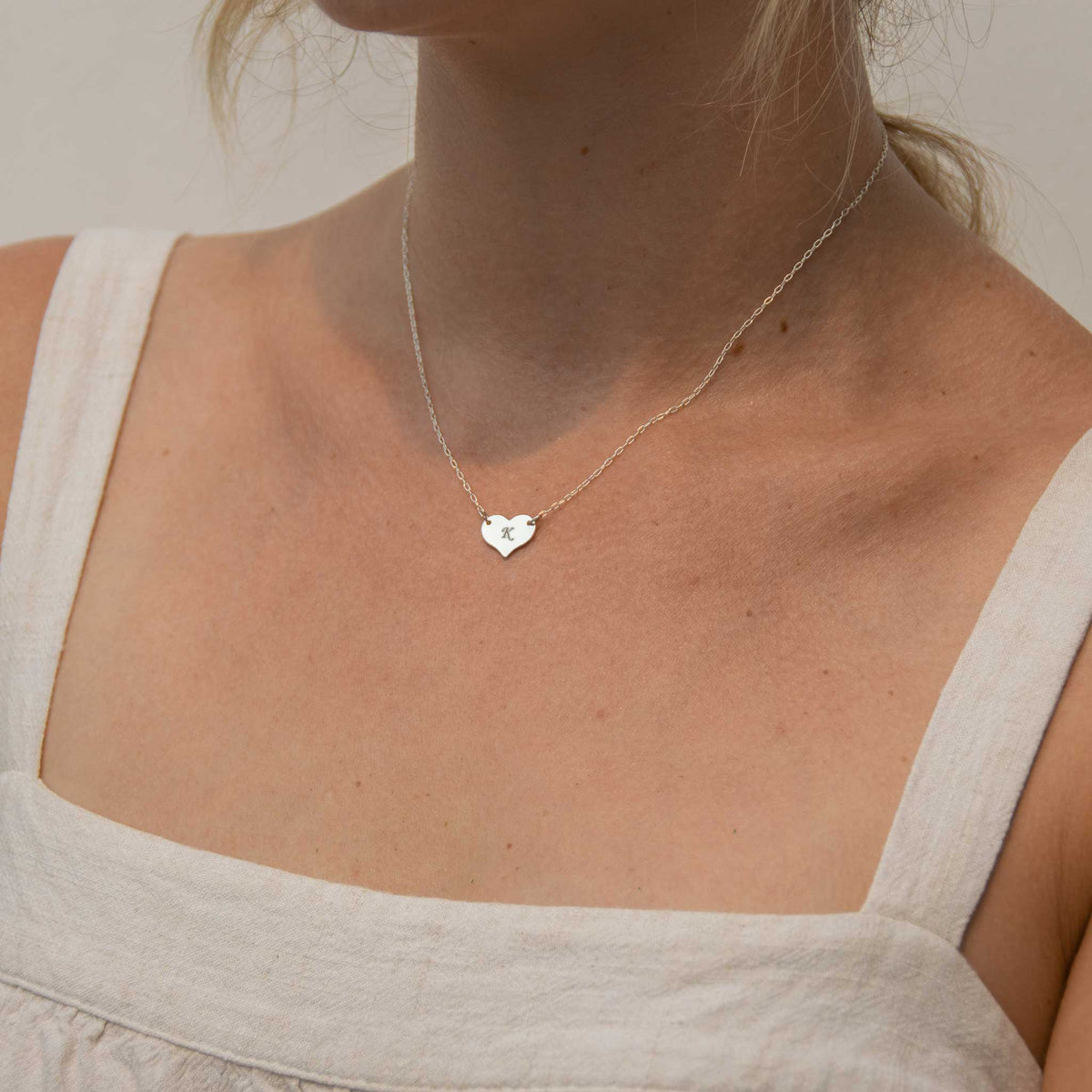 Woman wearing the heart pendant necklace with a white tank top on. 