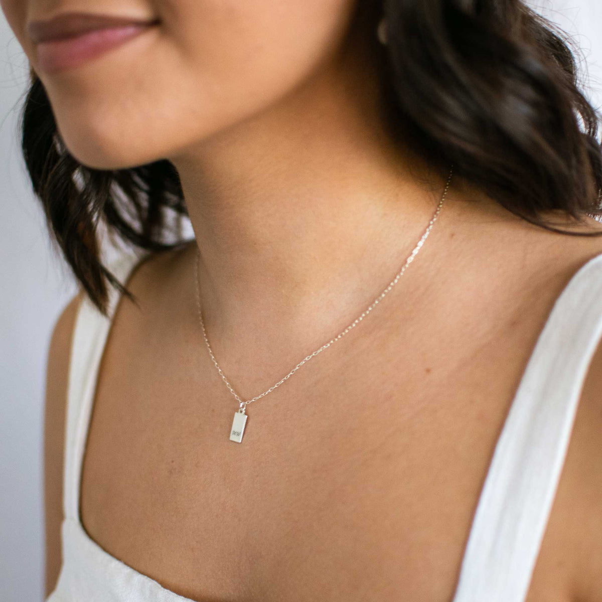 Model wearing a small silver tag necklace with mw engraved.