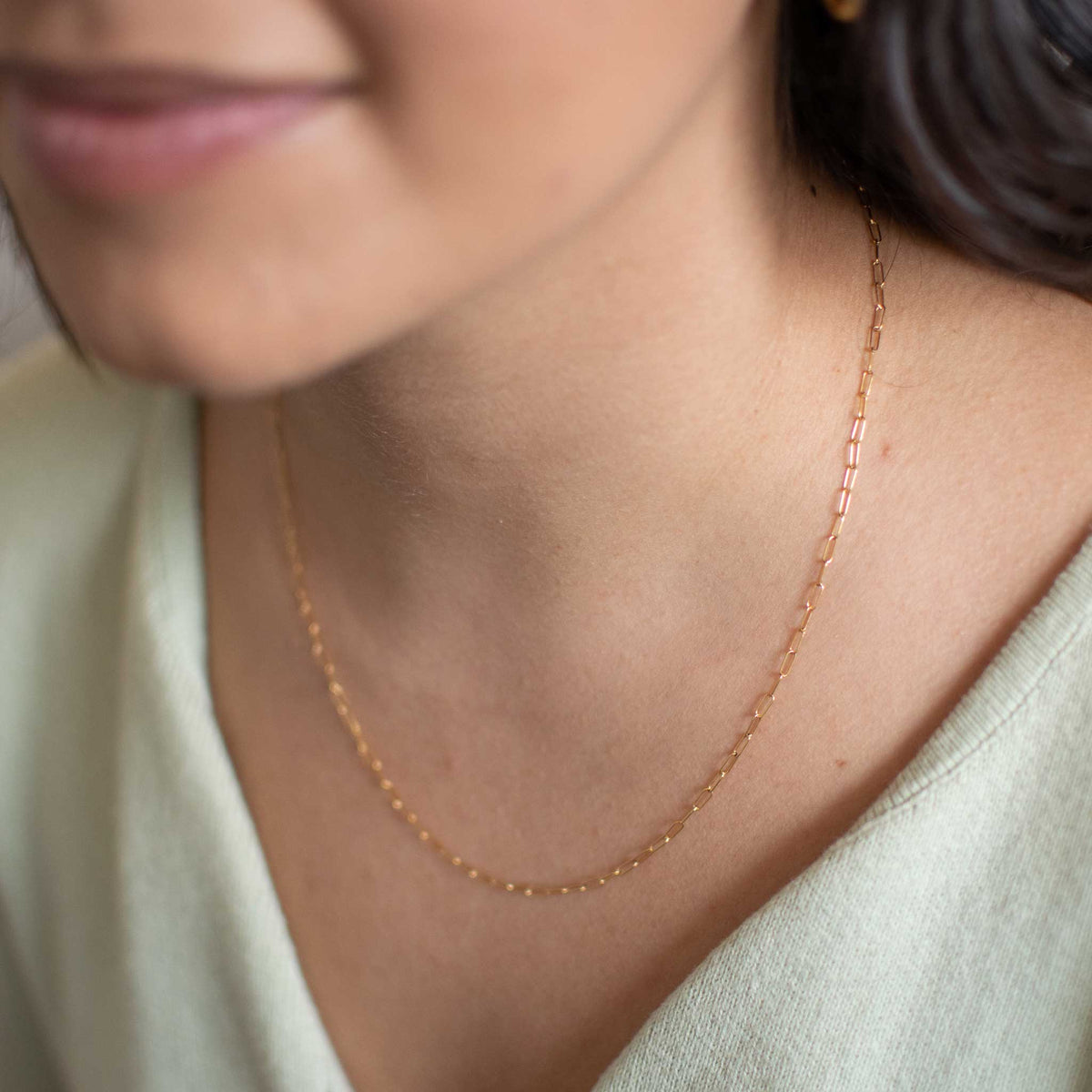 small gold link chain worn by a woman with the right side of necklace in focus. 